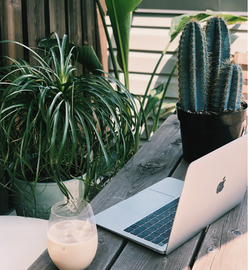 Remote work - featuring a Macbook and a drink on a table outdoors, surrounded by plants,
