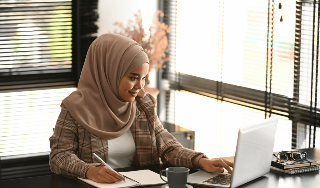 a woman wearing hijab working at her laptop and smiling