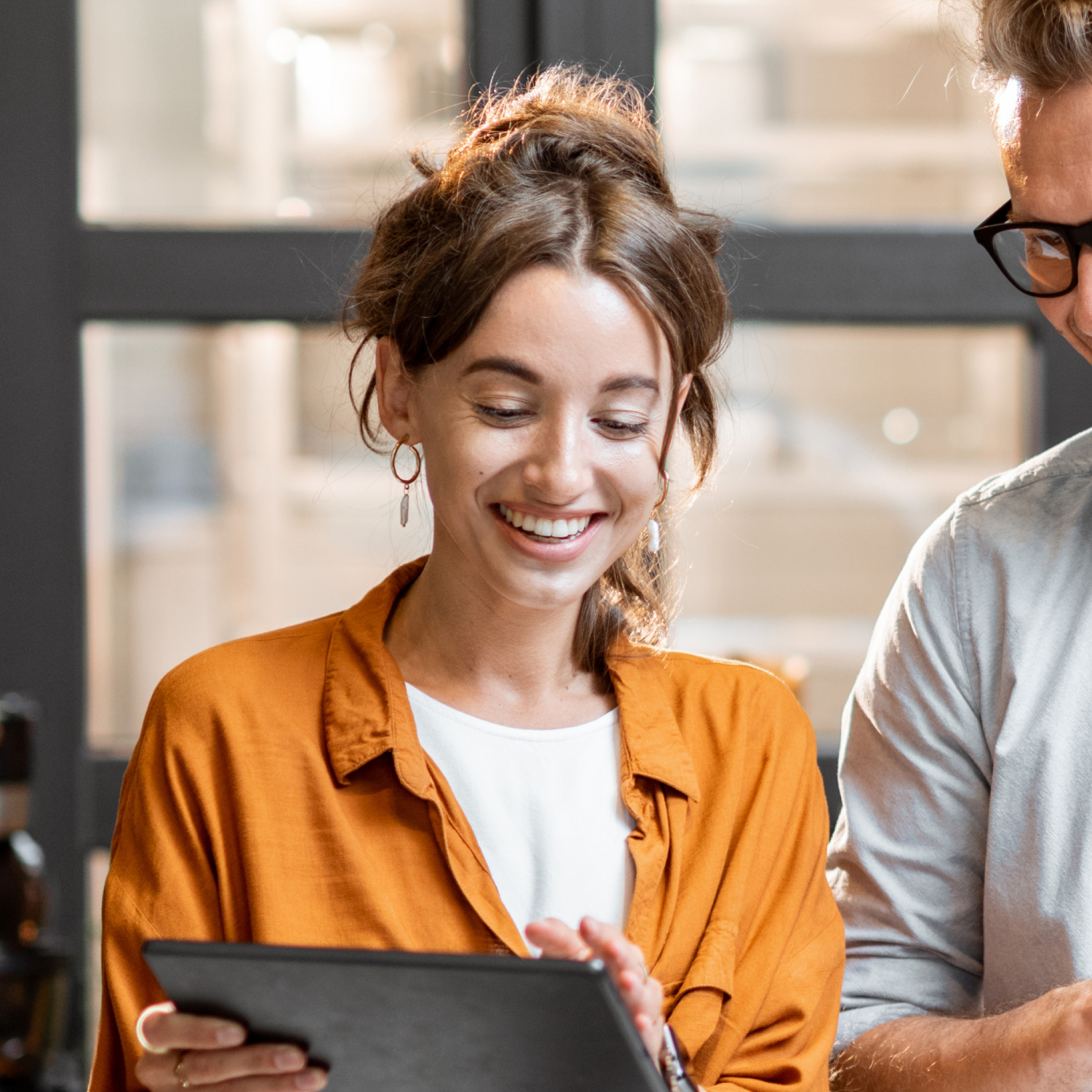 An image of a woman smiling as she show something to her colleague on her tablet