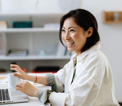 An image of a smiling woman, her hands lifted up from typing on a laptop