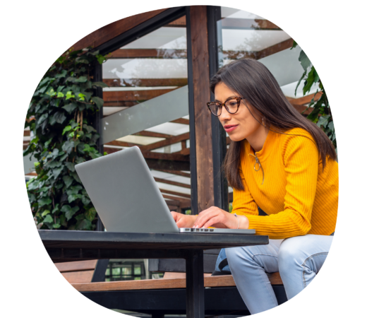 An image of a woman in bright yellow working outdoors, typing on her laptop