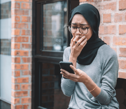 woman in anguish while looking at her phone and covering her mouth