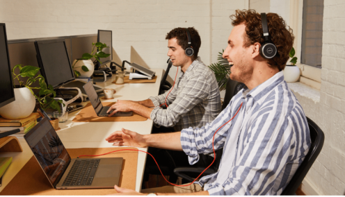Two men looking at laptops, wearing headsets