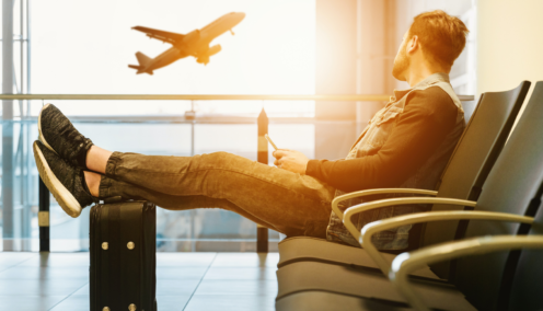 Man sits in airport terminal, feet up on a suitcase as he watched a plane take off outside the window