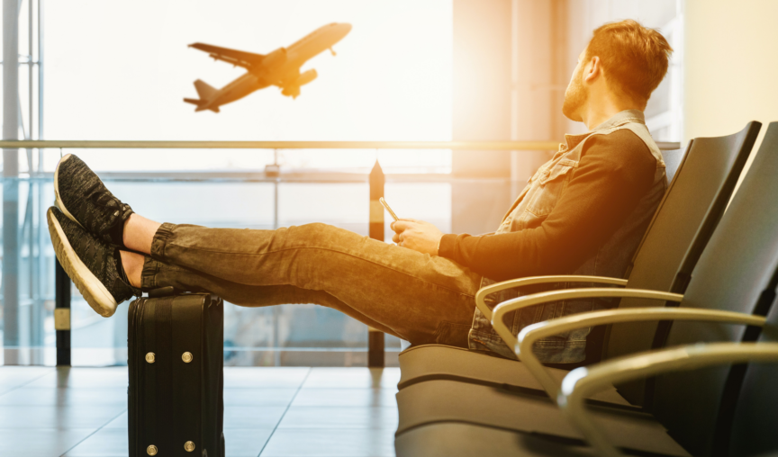 Man sits in airport terminal, feet up on a suitcase as he watched a plane take off outside the window