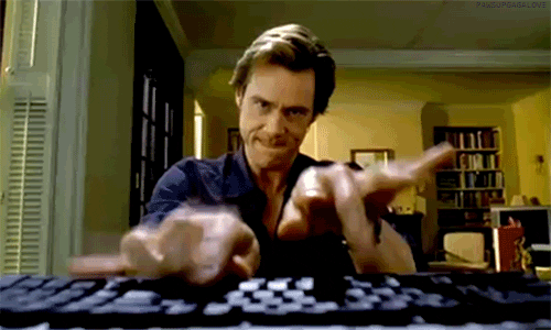 A person aggressively types on a keyboard, with a determined facial expression, inside a dimly lit room with shelves and a computer in the background.