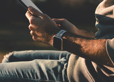 An image of man sitting outdoors holding a tablet and bathed in golden light