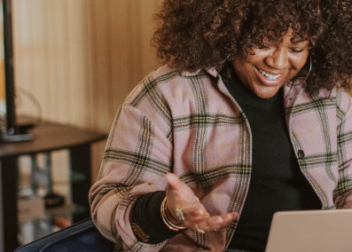 An image of a woman smiling as she looks down at her laptop