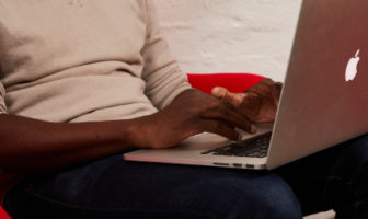 An image of a man sitting while typing on a laptop