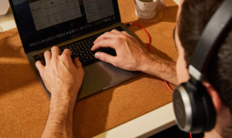 An image of a man wearing headphones while typing on a laptop