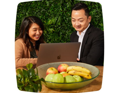 Two colleagues smiling as they discuss something on the laptop