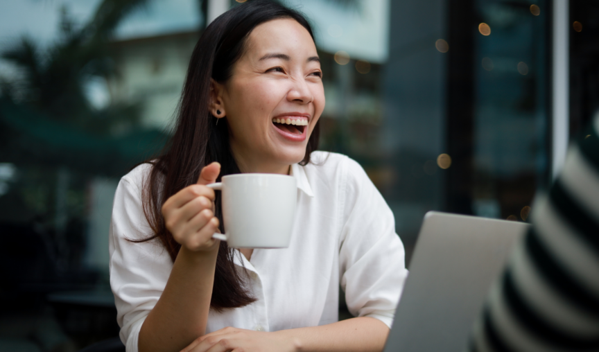 woman holding a cup of coffee and smiling while working in front of her laptop