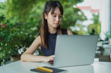 asian woman typing on her laptop in an outdoor space