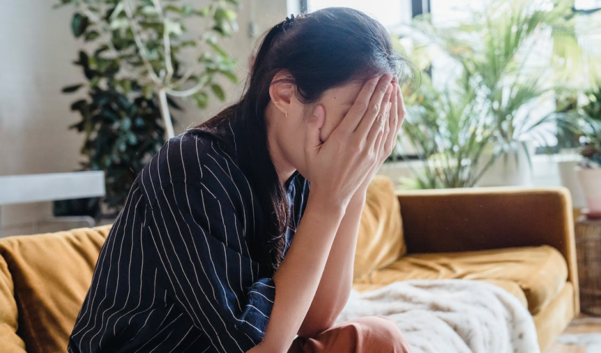 woman burying her face in her hands while seated on a sofa