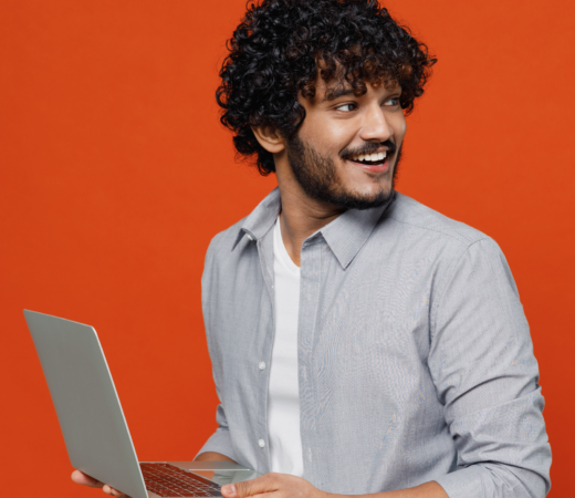 An image of a man smiling to his left as he holds a laptop