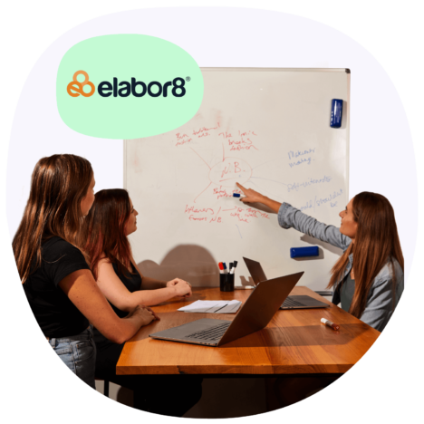 An image of a woman pointing to a whiteboard and showing it to two women, a laptop on the table. There is a logo of elabor8 on the upper right corner