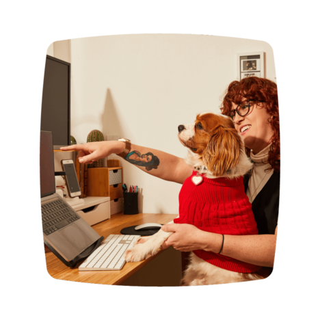 A woman holding her dog and showing something on the laptop screen