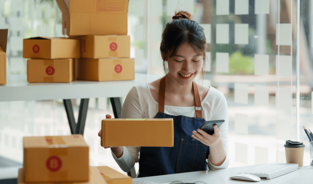 a woman smiling at her phone while holding a package at work