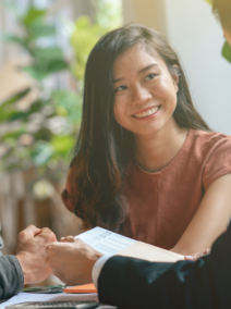A smiling couple sits across from a professional in a business setting, engaging in a friendly discussion.