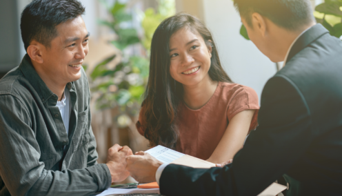 A smiling couple sits across from a professional in a business setting, engaging in a friendly discussion.