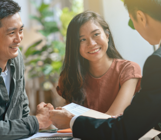 A smiling couple sits across from a professional in a business setting, engaging in a friendly discussion.