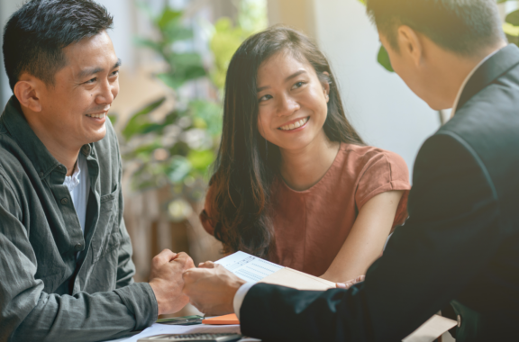 A smiling couple sits across from a professional in a business setting, engaging in a friendly discussion.