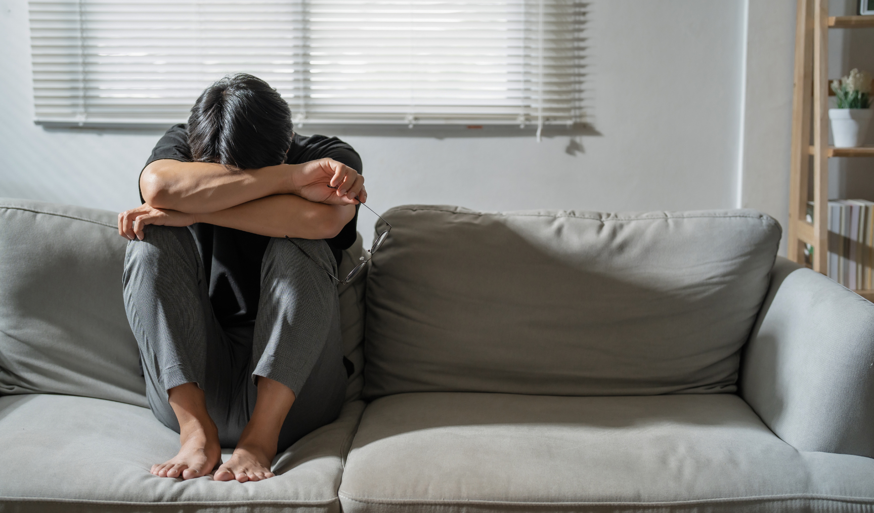 man huddled on his sofa hugging his legs with his head down