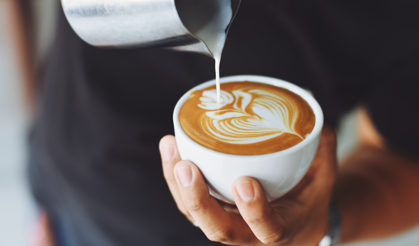 man pouring milk into a coffee cup to create latte art