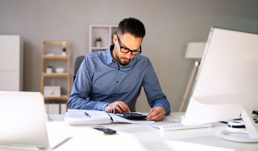 man seated at his desk punching numbers into a calculator