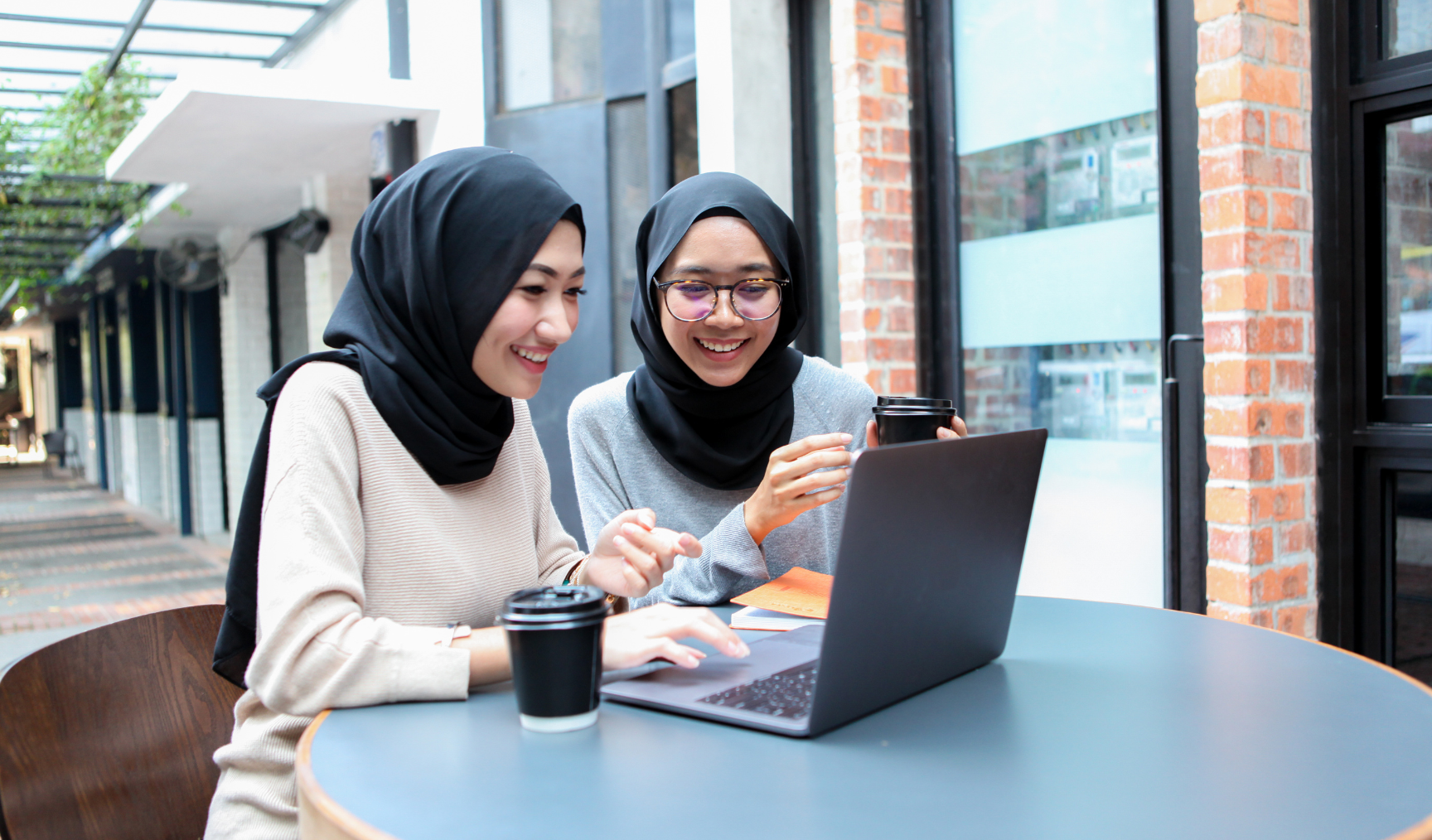 two women smiling and discussing something over their laptop