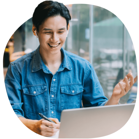 An image of a man smiling as he takes notes and looks at his laptop