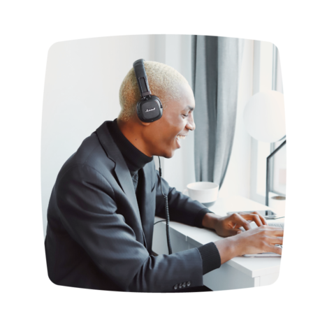 An image of a man wearing headphones smiling as he types on his laptop