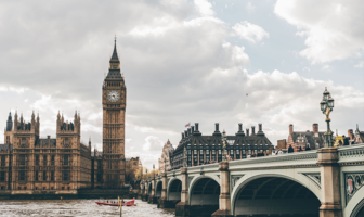View of Big Ben and the Houses of Parliament in London, with Westminster Bridge spanning the River Thames under a cloudy sky.