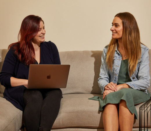 A photo of two women sitting on a couch, smiling and engaged in a conversation