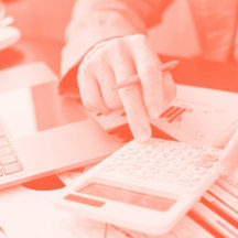 Person using a calculator at a desk with a laptop and financial documents, tinted in red.
