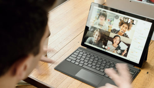 Remote Meetings. Person participating in a video call on a tablet, showing four other people on the screen in a virtual meeting.