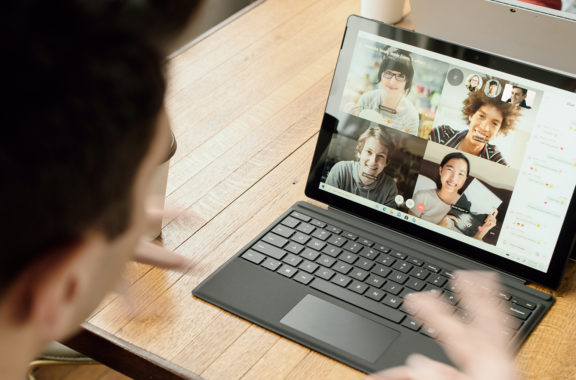 Remote Meetings. Person participating in a video call on a tablet, showing four other people on the screen in a virtual meeting.