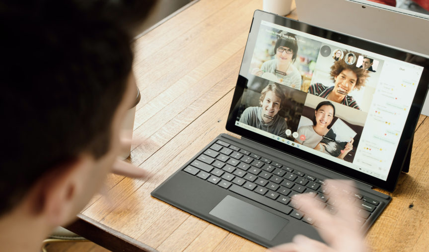 Remote Meetings. Person participating in a video call on a tablet, showing four other people on the screen in a virtual meeting.