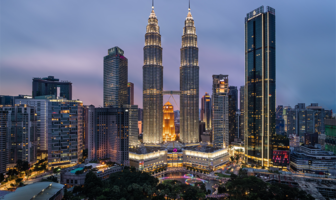 Night view of the Kuala Lumpur city skyline, featuring the illuminated Petronas Twin Towers surrounded by modern high-rise buildings under a twilight sky.