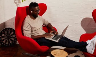 guy seated on a loungechair smiling and using his computer