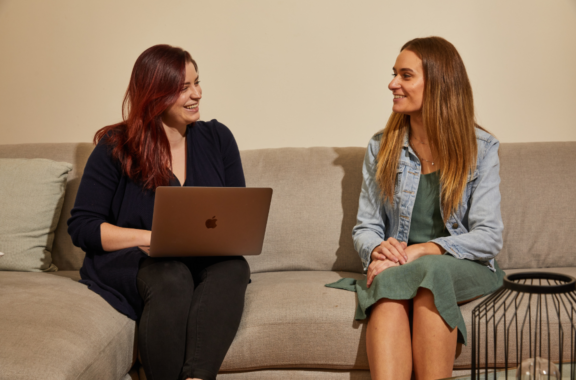 two women sitting on a sofa with an laptop