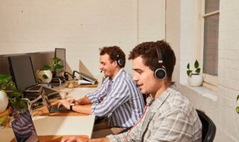 Two men wearing headphones working at laptops in an office setting