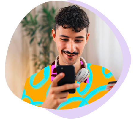 A smiling man with headphones around his neck, wearing a bright patterned shirt, looking at his phone