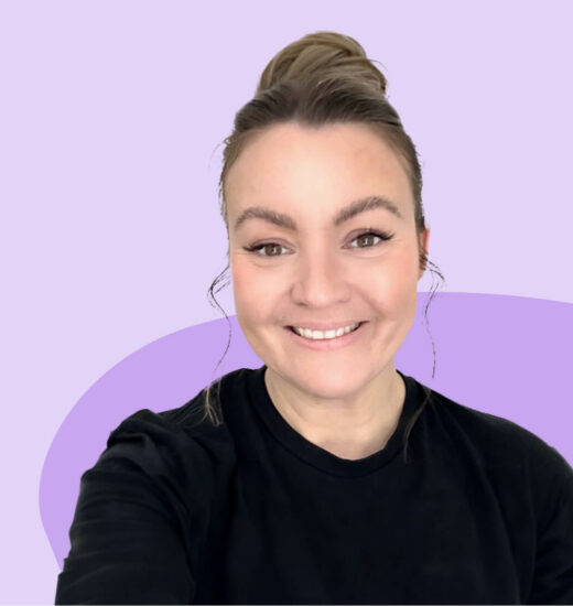 A woman with her hair tied up in a bun, smiling warmly at the camera. She is wearing a black top against a light purple background with a darker purple accent in the shape of a curve behind her.