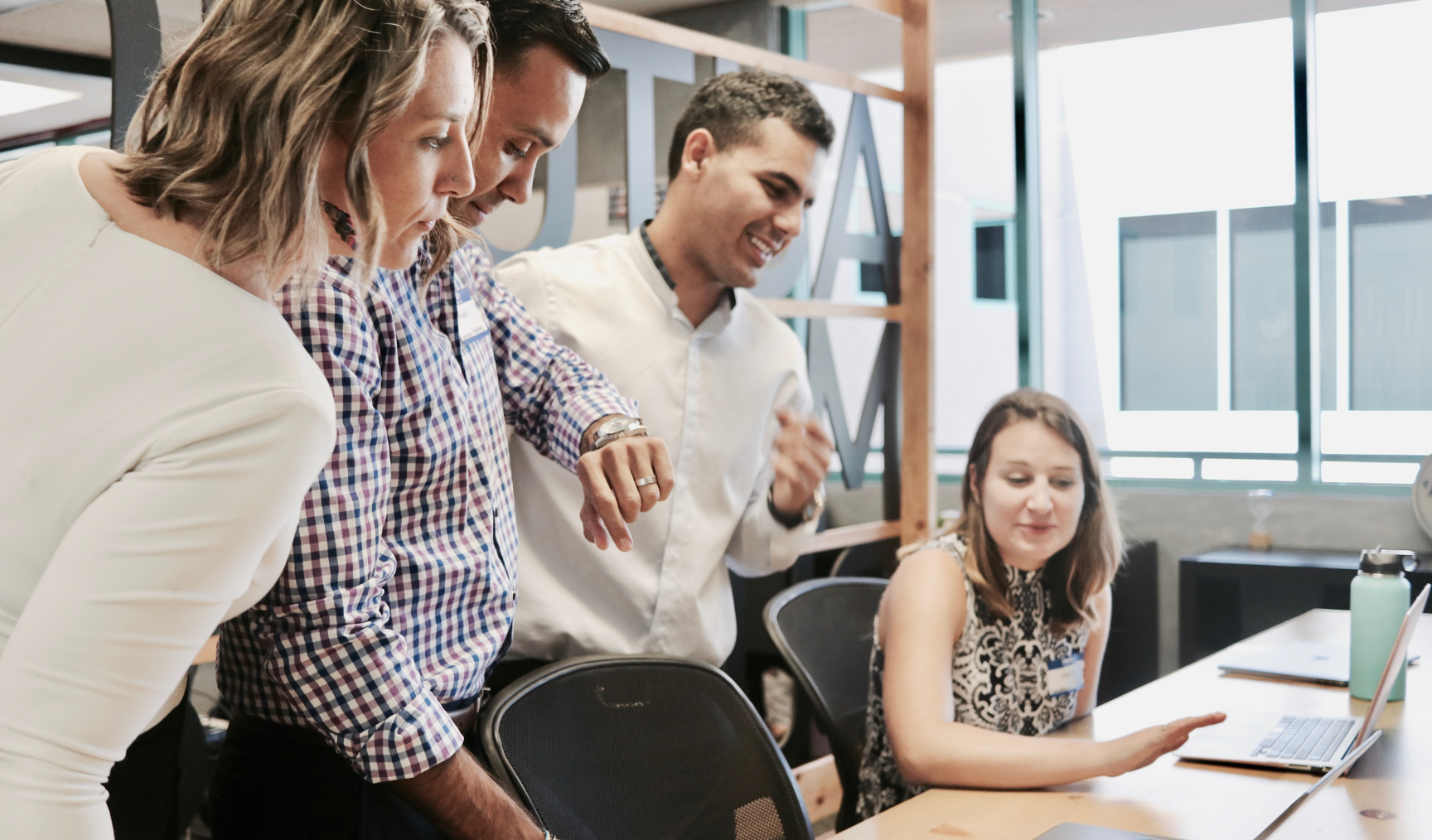 A woman sits at her desk while her colleagues chat to her
