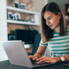 A woman in a striped shirt working on a laptop at home, with a focused expression, suggesting remote work or online learning