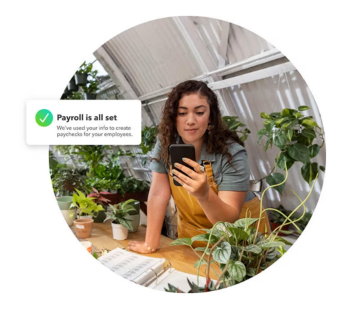 A photo of a woman in a greenhouse setting, surrounded by plants, looking at her smartphone. A digital overlay displays a notification saying, "Payroll is all set,"